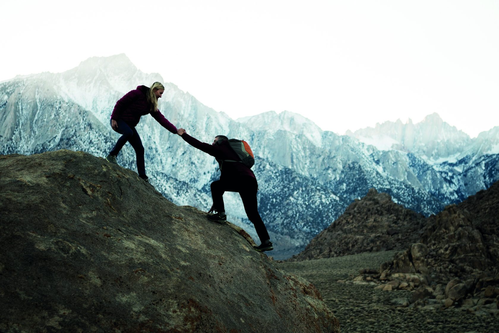 Happy couple hiking while one helps the other up  a steep cliff